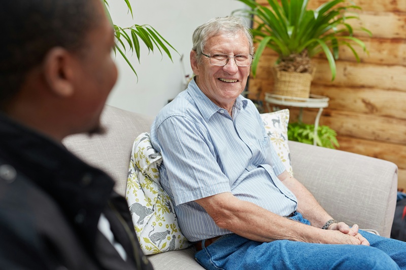 Two men sitting on couch smiling | home care vs. assisted living in Philadelphia | Neighborly Home Care