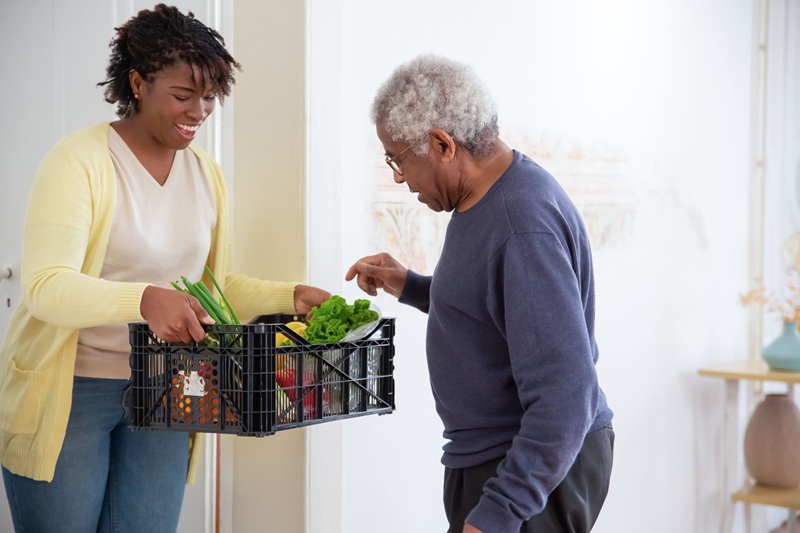 Woman holding plastic crate with vegetables | signs elderly parent needs care | Neighborly Home Care